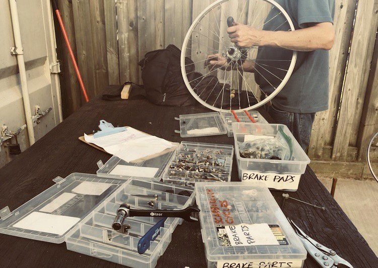 A table with bicycle repair parts and tools, and a person holding a bike wheel