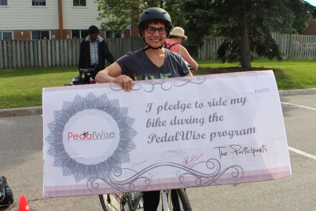 Person with a helmet holding a large sign that says 'I pledge to ride my bike during the PedalWise program'.